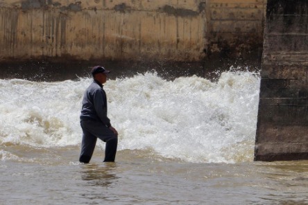 上游水电站泄洪，下游的河滩上还有老人捡石头……